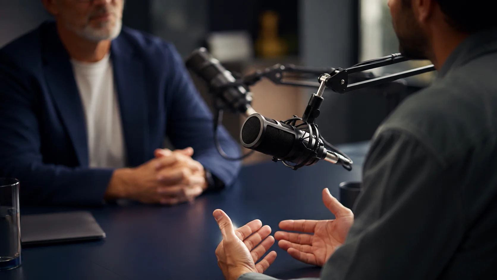 Zwei Personen sitzen sich in einem Studio gegenüber; ein professionelles Mikrofon steht im Mittelpunkt des Gesprächs.